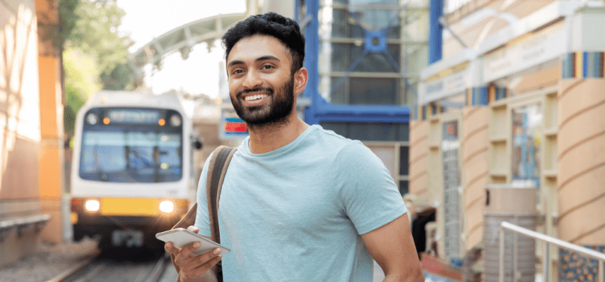 A woman walking stops to look at her mobile device. She's standing on a street sidewalk.