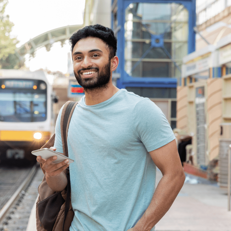 A woman walking stops to look at her mobile device. She's standing on a street sidewalk.